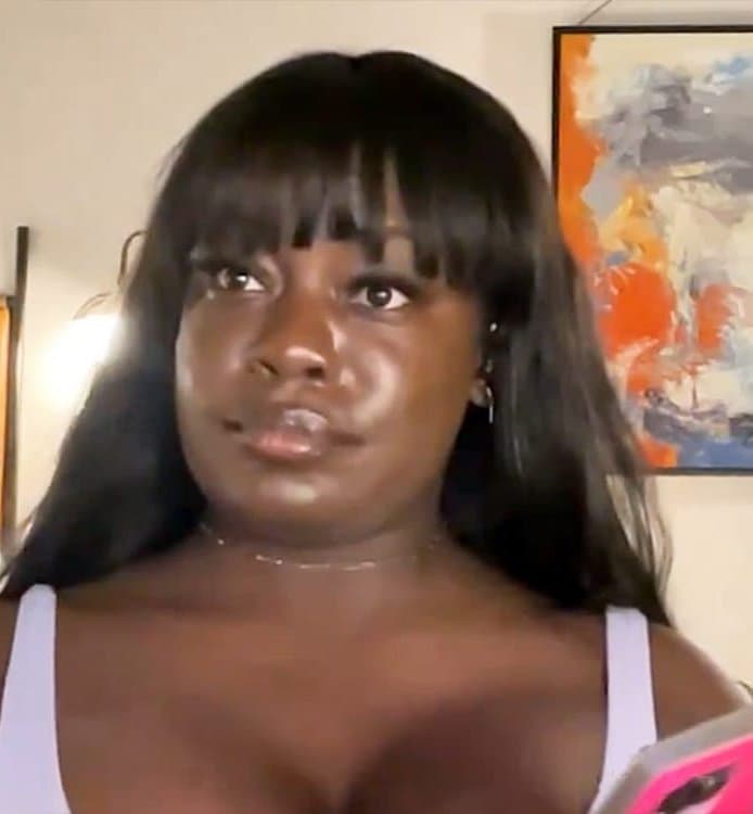 Dr. Raven Baxter, with long dark hair and bangs, looks into her phone camera in a room in front of an abstract orange and blue painting