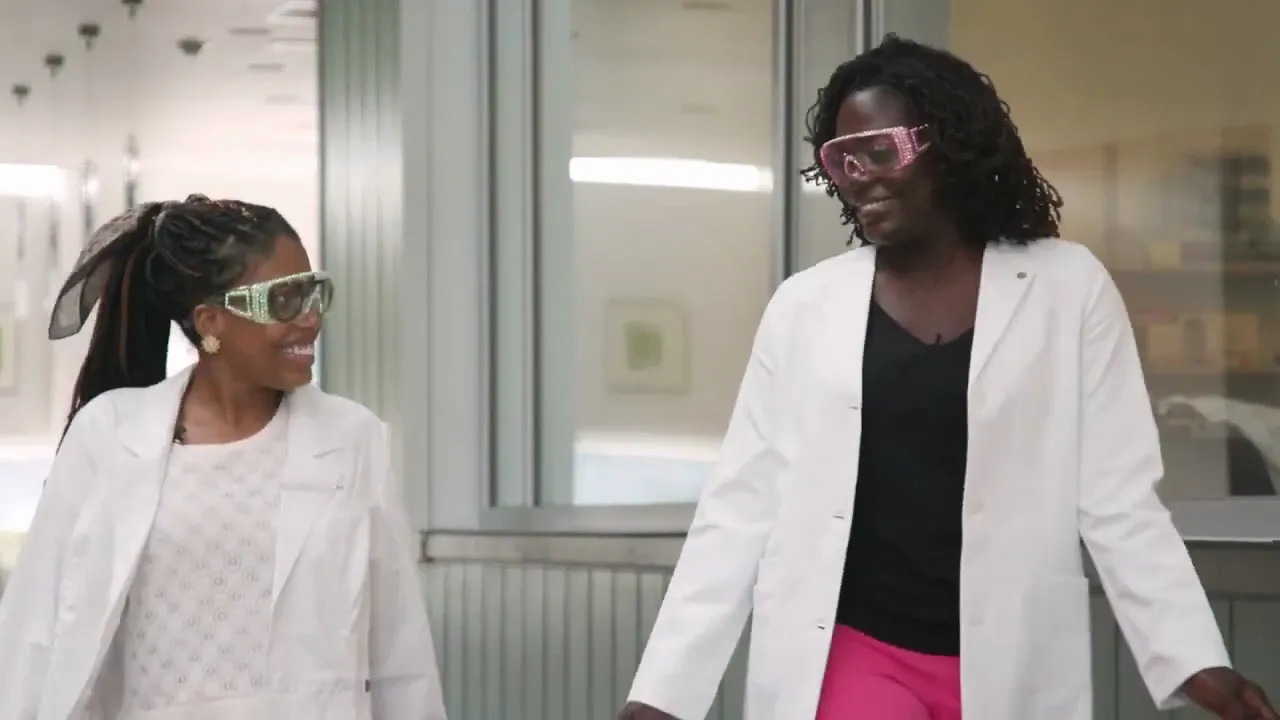 Dr. Raven Baxter smiling in a lab coat and pink goggles beside Sydney Anderson, from Nerdy Jobs Episode 1