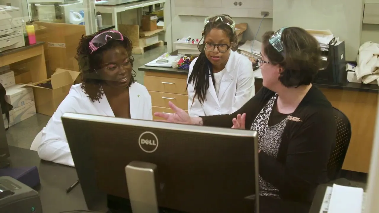 Dr. Raven Baxter looking over protein crystal images on a monitor with Sydney Anderson and Dr. Sarah Bowman, from Nerdy Jobs Episode 1