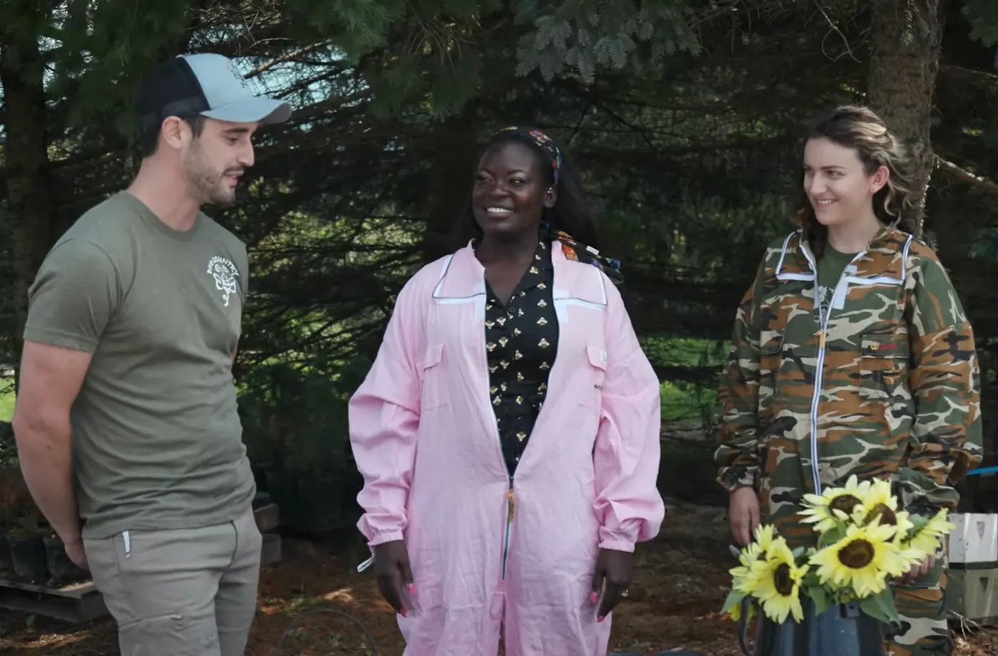 Dr. Raven Baxter in a pink beekeeping suit talking with two people beside a bucket of sunflowers, from Nerdy Jobs Episode 2