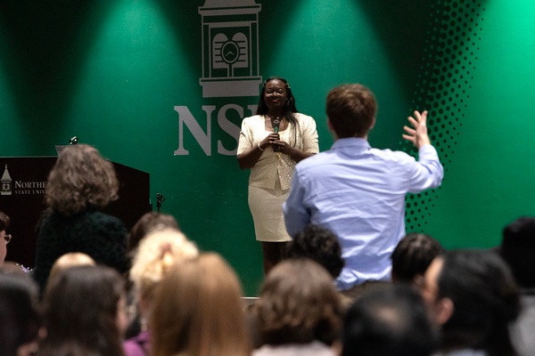 Dr. Raven Baxter speaking with a microphone to an audience at Oklahoma Research Day, Northeastern State University